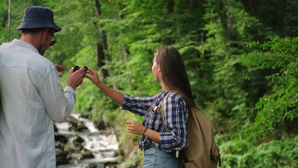 Backpacking Tour in Woodland Man and Woman are Viewing Waterfall alt
