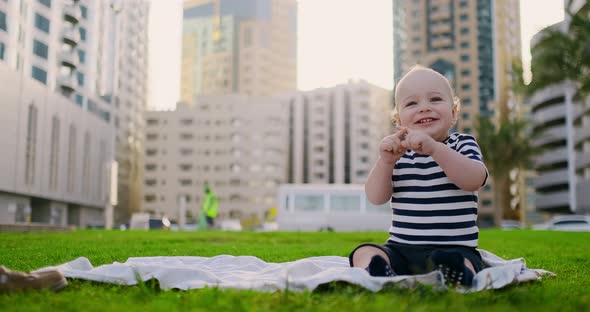 Happy Small Child Sitting in Grass with White Daisies City Background alt