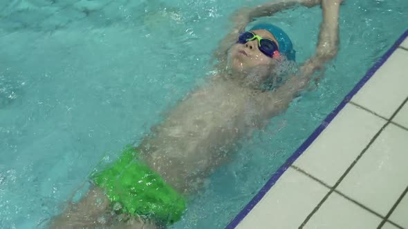 Little Caucasian Boy Wearing Goggles Swimming the Backstroke in a Pool