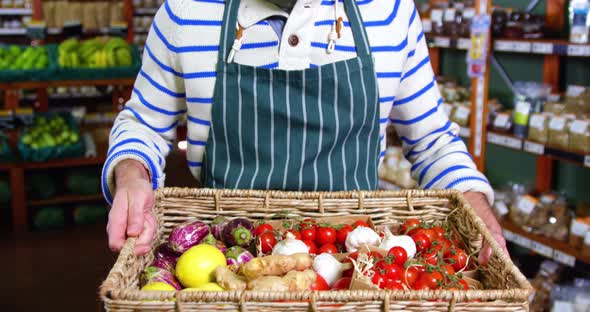 Smiling male staff holding basket of vegetables in organic section alt