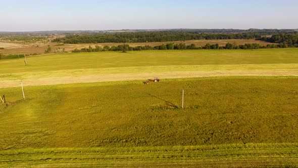 The tractor is stacking haystacks on an agricultural field in autumn, aerial view alt