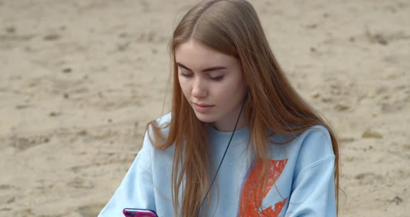 Young Beautiful Girl Sitting on the Beach and Holding a Telephone in her Hands