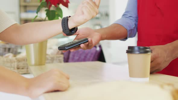 Video of hands of biracial woman paying with smartwatch for baguette alt