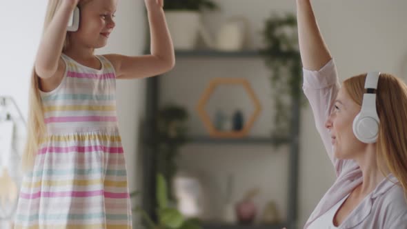 Happy Girl and Pregnant Mother in Headphones Dancing in Kitchen alt