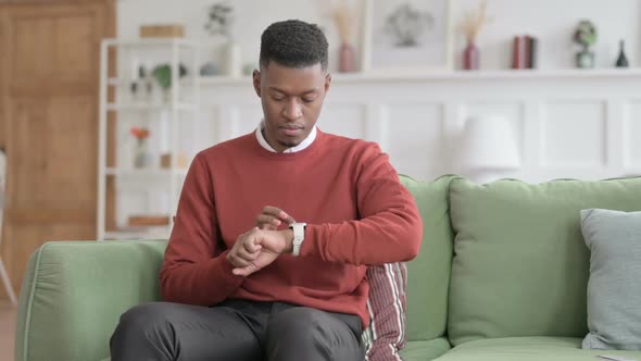 African Man using Smart Watch while Sitting on Sofa alt