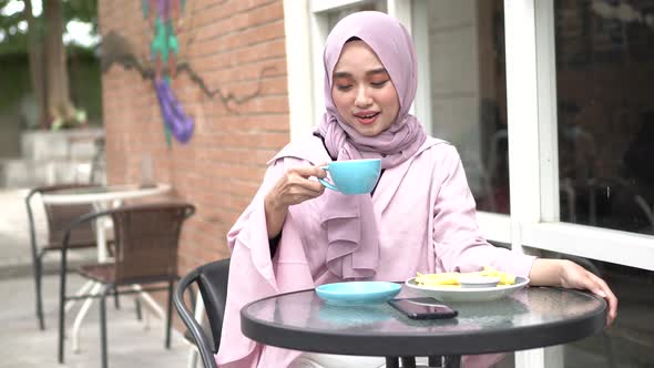 happy Asia hijab woman drink coffee while sitting at cafe