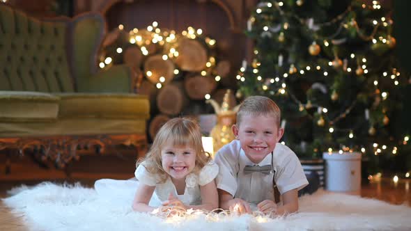 Happy children lie on the floor against the background of a festive Christmas tree alt