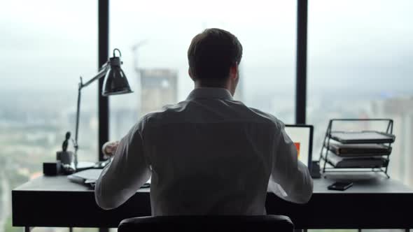 Businessman Reading Papers at Workplace. Manager Looking at Graphs on Laptop alt