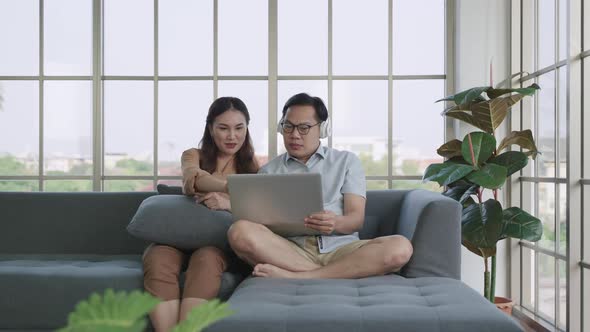 husband and wife using calculator laptop computer talking doing paperwork together sit on sofa