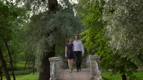 Two Young People in Love Walk Through a Small Bridge in the Park Above the Lake alt
