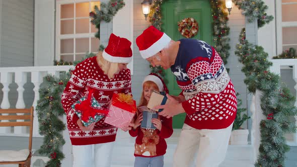 Senior Grandparents with Grandchild Girl Kid Exhcanging Gifts Near Christmas House Celebrating Xmas alt
