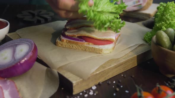 Making the Sandwich with Sliced Bacon, Pickle and Vegetables on the Wooden Board in the Beam alt