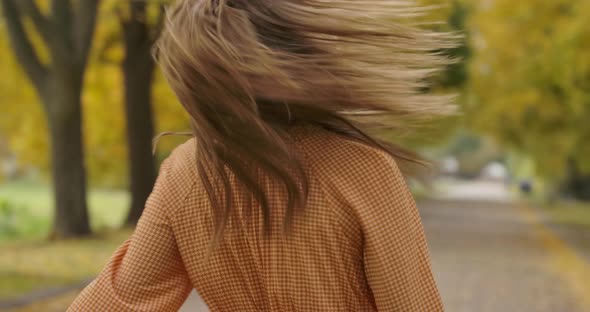 Smiling Caucasian Woman with Long Brown Hair and Green Eyes Spinning in the Autumn Park alt