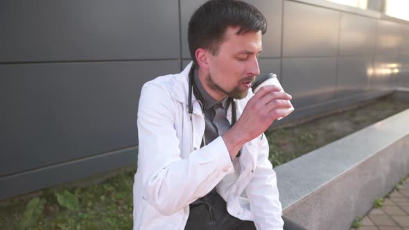 Handsome Caucasian Doctor Exchanging Medical Documents for Cup of Coffee in Disposable Cup. Tired alt