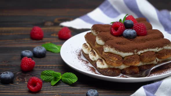 Portion of Classic Tiramisu Dessert with Raspberries and Blueberries on Wooden Background alt