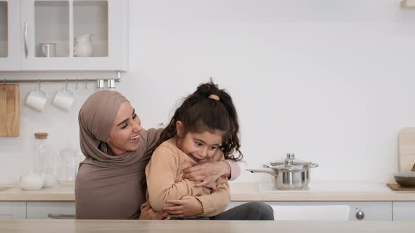Joyful Muslim Mother Tickling And Hugging Little Daughter In Kitchen alt
