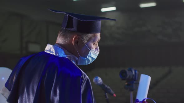 University Lecturer in Academic Clothes and Hat is Presenting Diplomas Using Modern Technologies Via alt