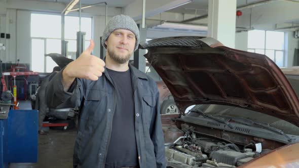 Mechanic in car repair shop showing thumbs up alt