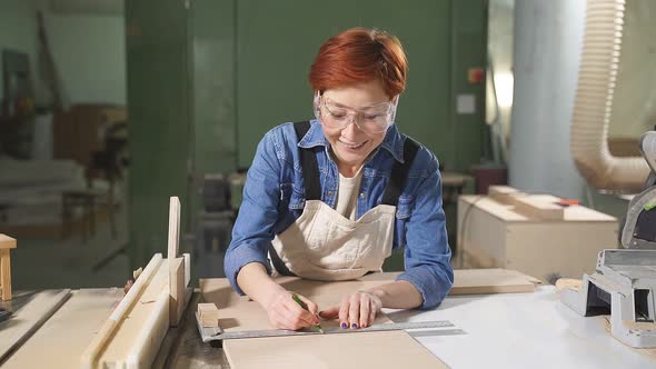 Redhead Young Female Carpenter Working As Wood Designer in Small Carpentry Workshop