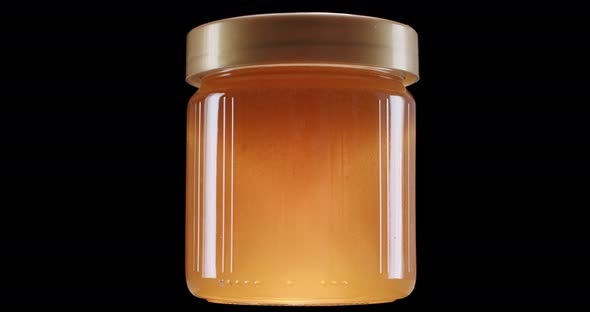 Glowing honey jar on black background, static shot. Honey jar starts to glow, delicious honey insid alt