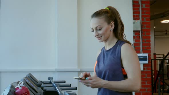 Girl Running on Treadmill and Uses Smartphone