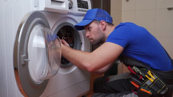 Working Man Plumber Repairs a Washing Machine in Home alt