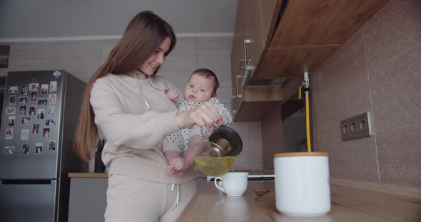 Mom With A Small Child In Her Arms Brews Tea In The Kitchen