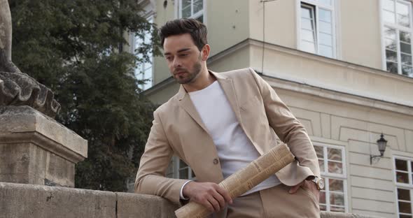 Young Man Standing With A Newspaper In His Hands Near The Fountain alt