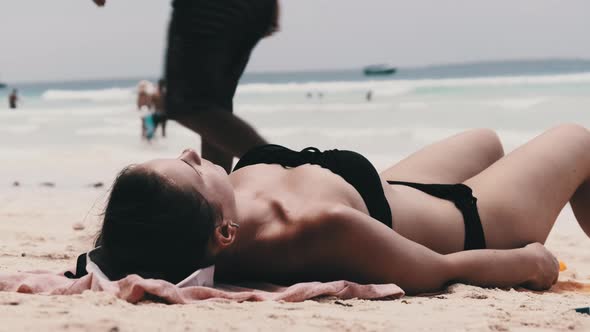 Young Woman Sunbathes on a Paradise Sandy Beach Lying in Black Bikini Near Ocean alt