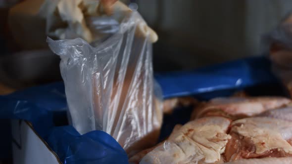 Macro View of Hands in Gloves Packing Chicken Legs From a Box Into Individual Plastic Bags alt