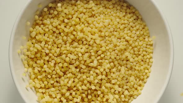 Couscous grains falling into a white bowl