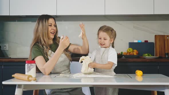 Little Girl with Mother Kneads Raw Dough at Table in Kitchen alt
