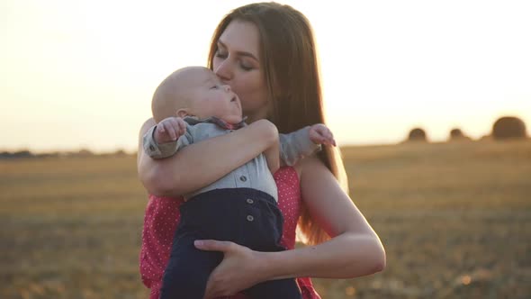 Mother Caresses Whirls and Embraces Baby Son with Harmony in Hay Field at Sunset alt