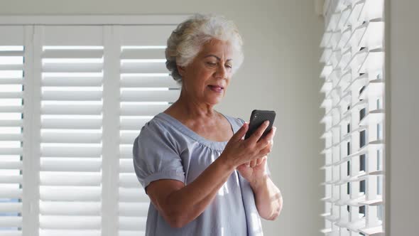African american senior woman using smartphone and looking out of the window at home alt