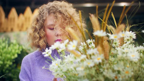 Young Woman with Blond Curly Looking Blooming Chamomile in Orangery alt