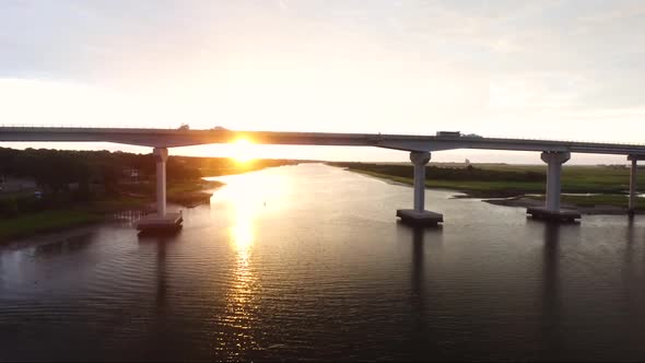 Flying towards bridge in Sunset Beach NC at sunrise while cars drive over it alt