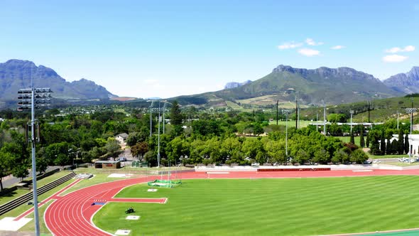 Aerial drone rotating tartan athletic track, athletes training sprints, mowing grass, university col alt