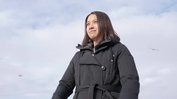 Young attractive woman in winter jacket stands outside and crosses her arms. Slow motion hero shot. alt