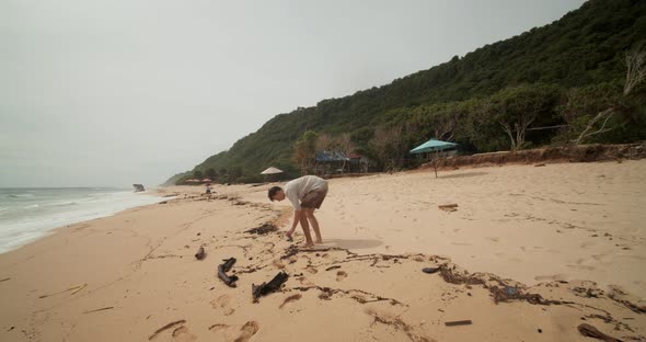 Young White Male Picking Up the Trash on a Sandy Beach in Bali alt