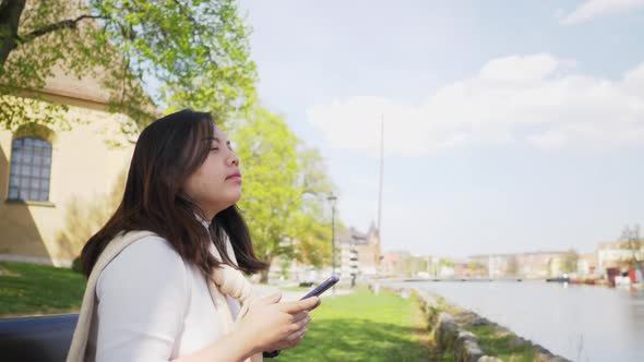 Asian woman sitting on a chair and spending time to use phone and take a deep breath at park alt