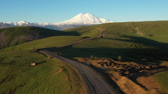 Top view of green field, winding roads and Caucasus mountains.Sunrise above Mount Elbrus alt
