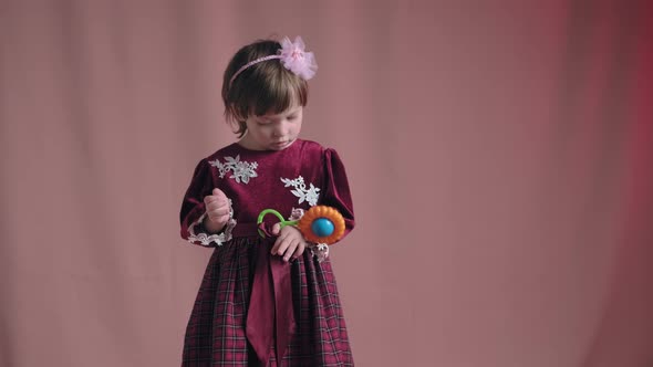 Cute Little Girl in an Vintage Burgundy Dress is Playing with a Rattle Toy