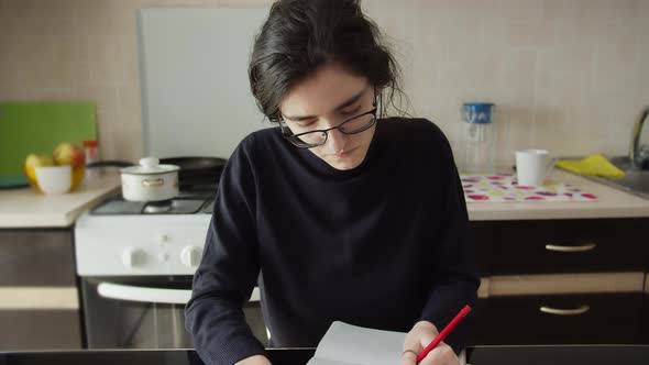 Brunette Serious Girl Sits in the Kitchen and Draws with a Pencil