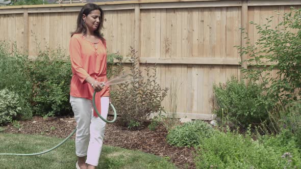 Woman in back yard watering plants with garden hose. alt