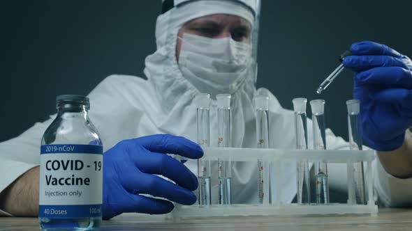 Scientist or Medical in Protective Kit Holding Test Tube with Covid-19 Vaccine. Coronavirus Vaccine alt