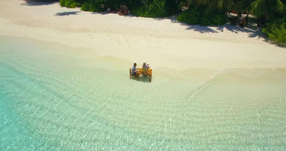 Aerial drone view of a man and woman eating breakfast on a tropical island beach. alt