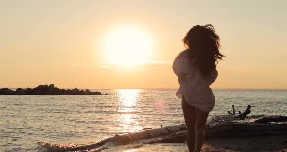 Young Brunette Woman in a White Shirt Running on the Beach at Sunset