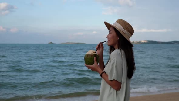 Slow motion of a beautiful asian woman holding and drinking coconut juice on the beach