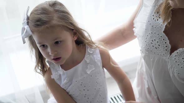 Beautiful Family Mother and Daughter in White Dresses are Sitting on the Floor By Large Window