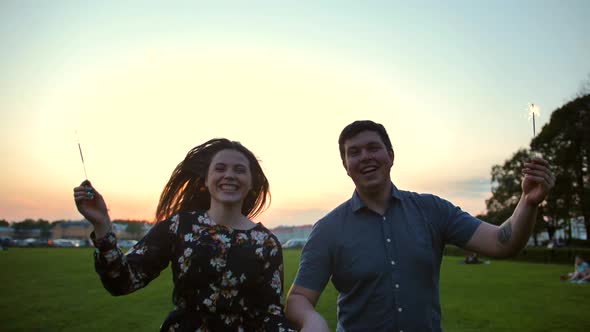 The Couple Running with Sparklers Sticks at Camera with Smile. alt